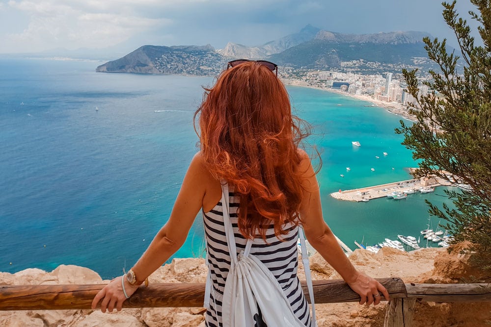 A woman is standing on a ledge, overlooking a beach in Calpe.