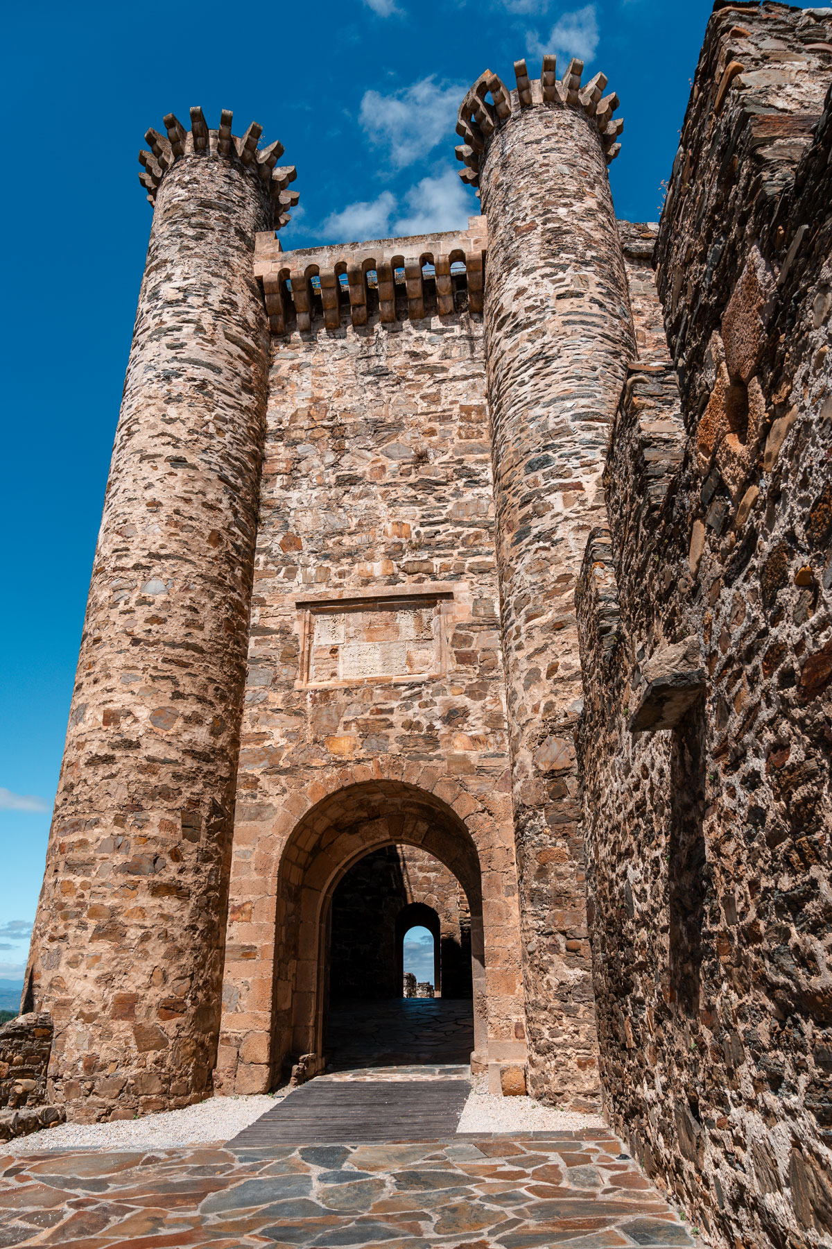 Castle stone walls, cylindrical towers and an arched entrance.