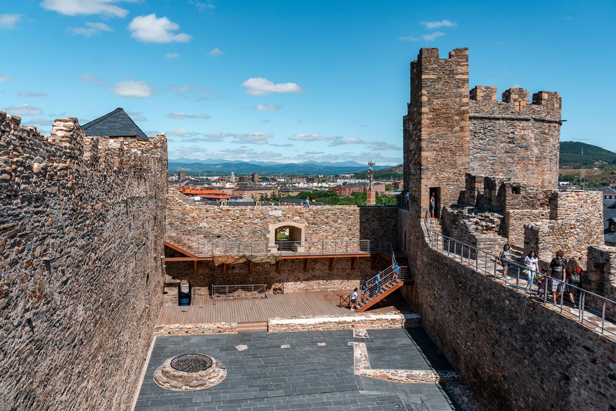 Visitor are exploring castle of Ponferrada, overlooking a city and mountains.
