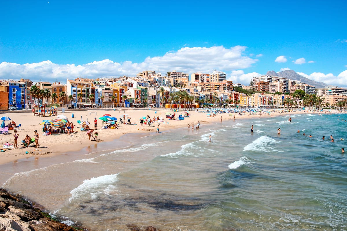 Busy Villajoyosa beach with colorful houses in the background.