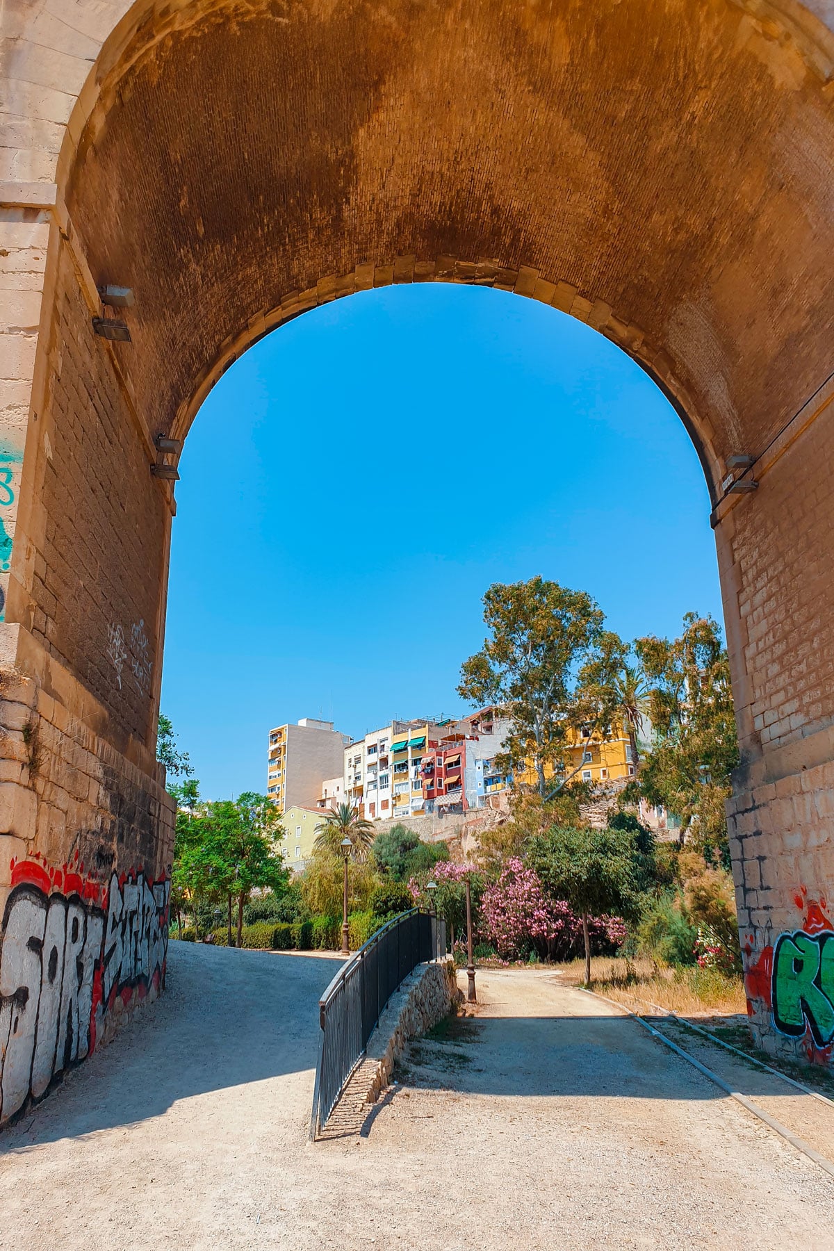 Bridge archway with graffiti and a view of colorful buildings.