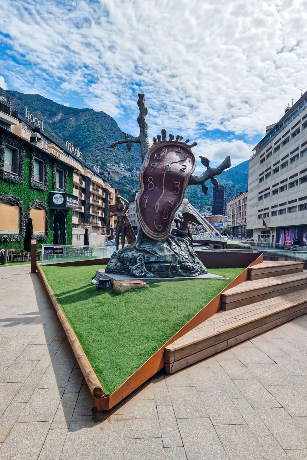 A surreal sculpture of a melting clock by Salvador Dali in a public square in Andorra la Vella, with mountains in the background.