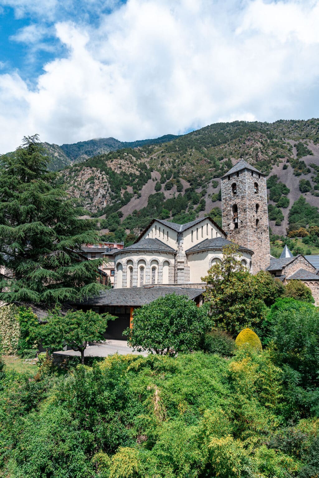 Sant Esteve historic stone church with a bell tower in Andorra la Vella, surrounded by lush greenery and mountains.