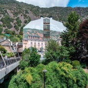 Riverside building covered with a huge mountain mural, backed by real hills in Andorra la Vella.