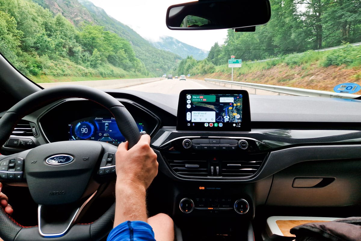 View from the driver’s seat while heading into Andorra through green mountains with navigation on the screen.