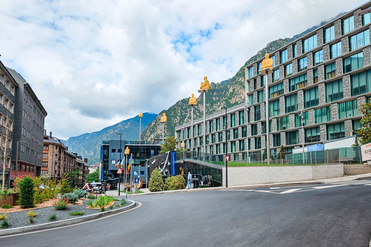 Contemporary hotel block lined with tall poles topped by golden seated figures in the Andorran capital.