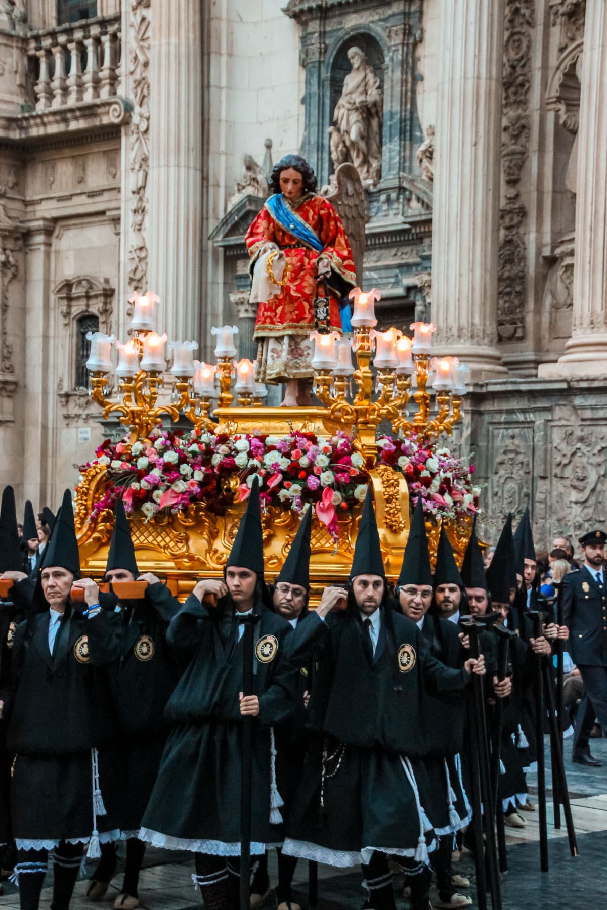 Holy Week procession with float and black-robed nazarenos in front of Murcia Cathedral.