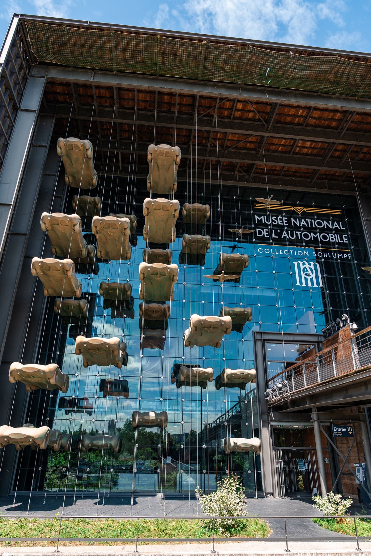Glass facade of the Musée National de l’Automobile in Mulhouse with car sculptures suspended on cables.