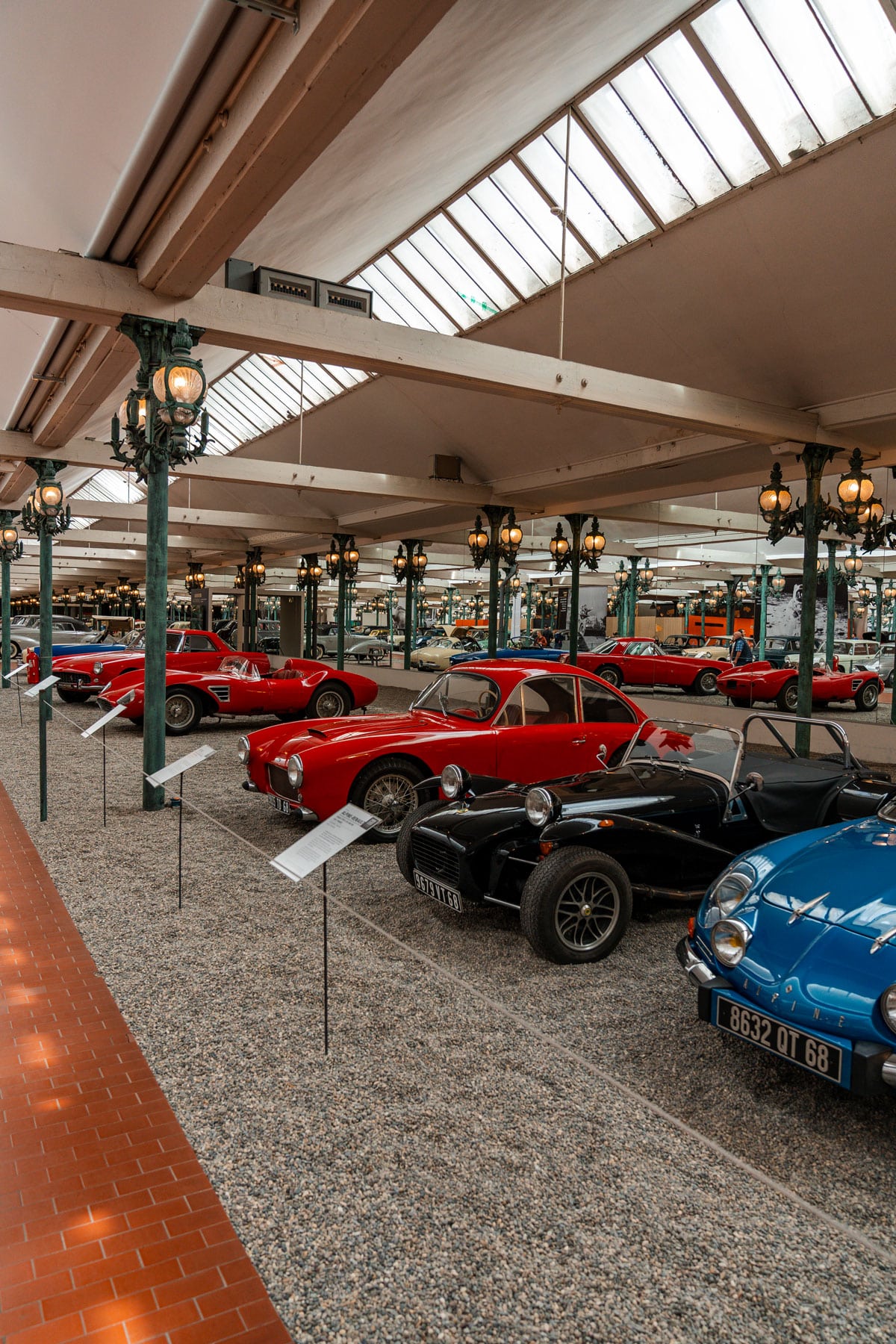 Rows of red and blue sports cars under ornate green lamp posts in the main hall.