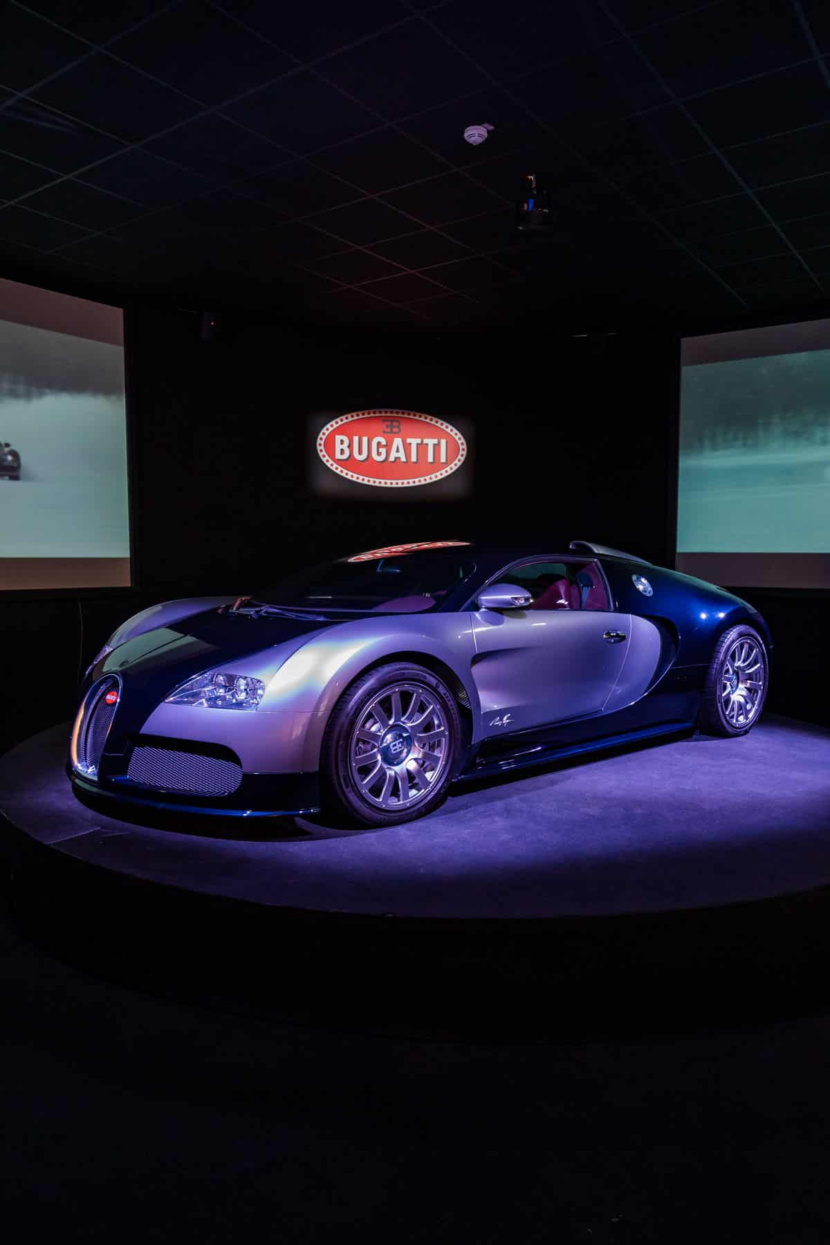 Modern Bugatti on a circular platform beneath the lit brand sign.
