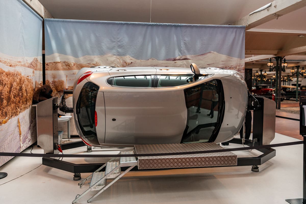 Silver car tipped on its side in the rollover simulator with metal steps up to the platform.