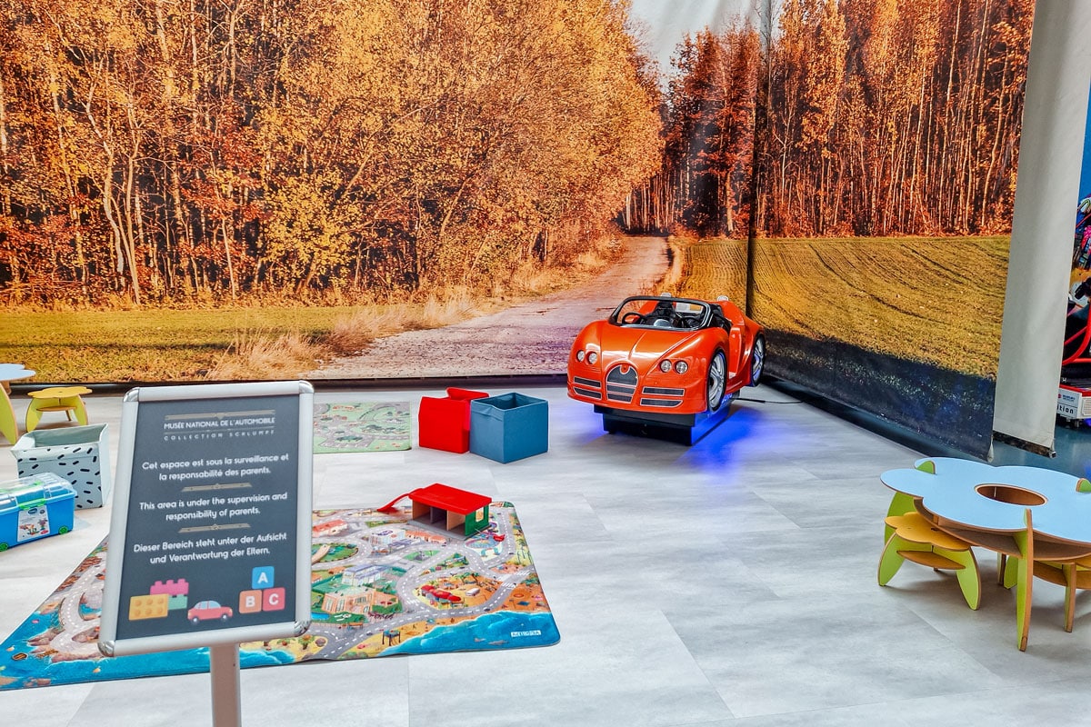Children’s play area with an orange ride-on car, road-print play mats and small tables.