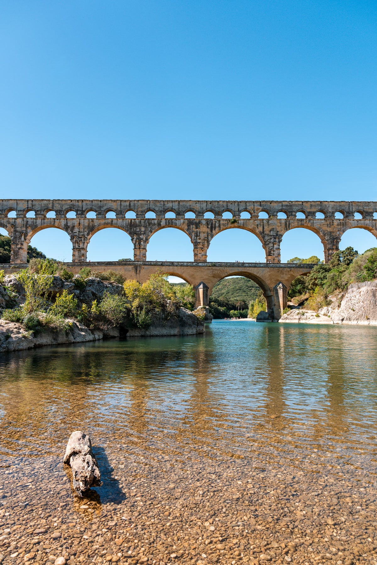 Pont du Gard aqueduct reflected in the river on a sunny day.