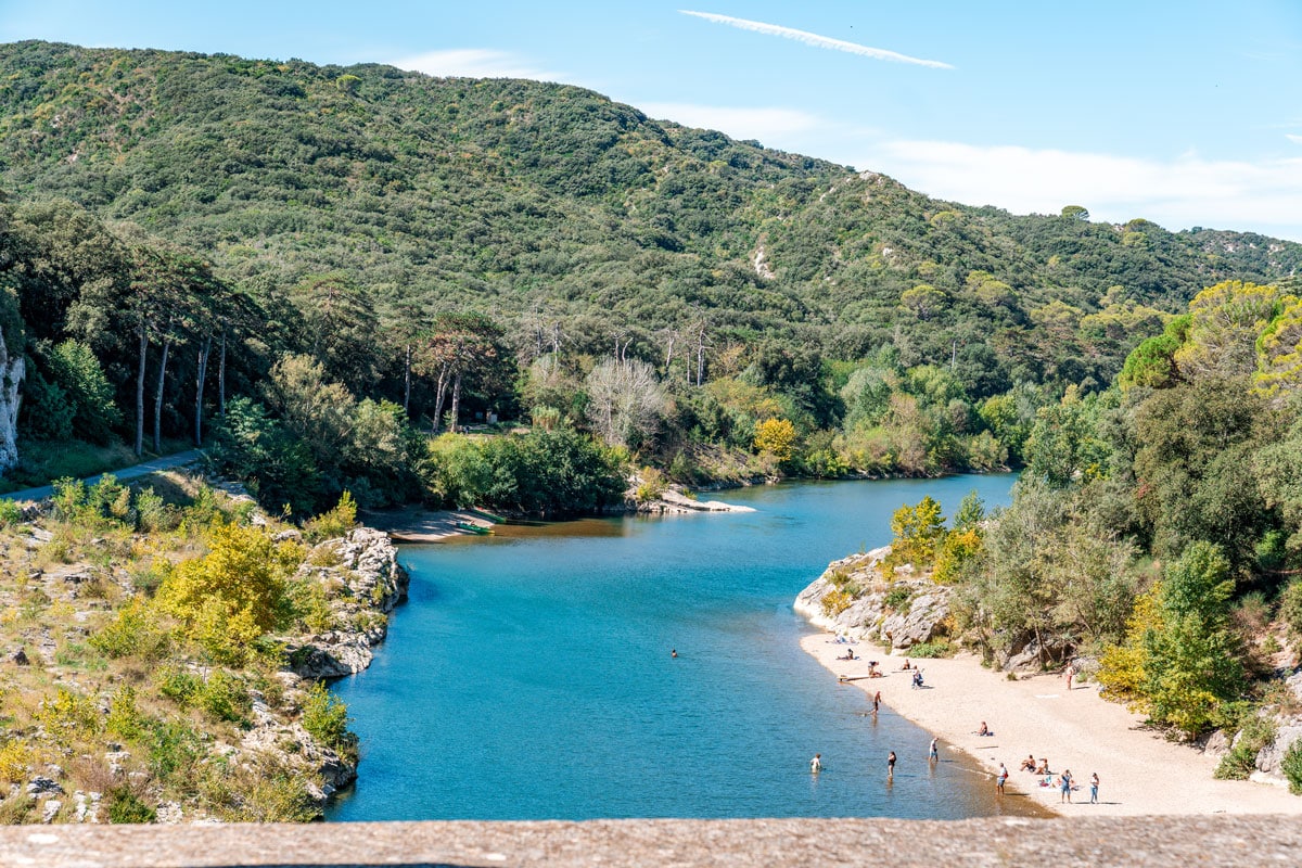 People relaxing on the pebble riverbank below Pont du Gard.