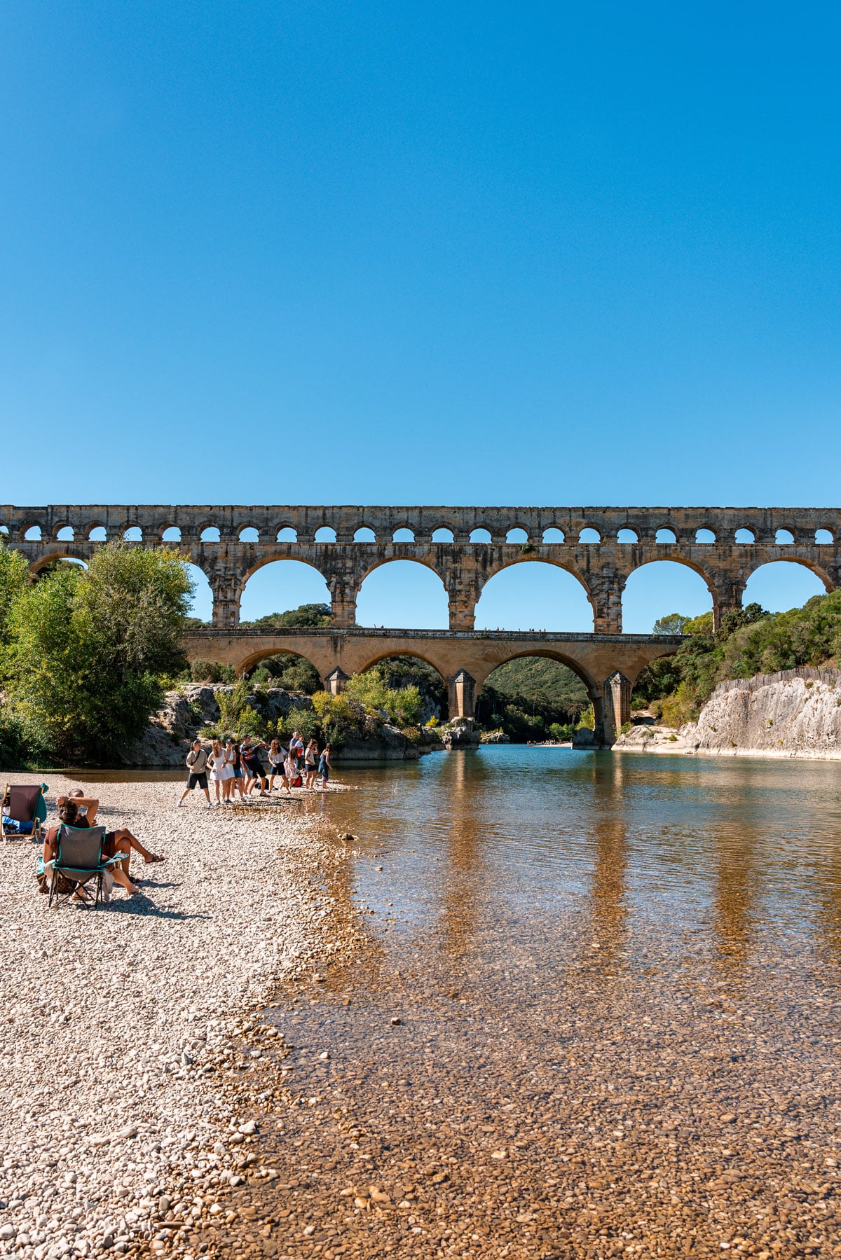 People in and around the river near the pebble bank below Pont du Gard.